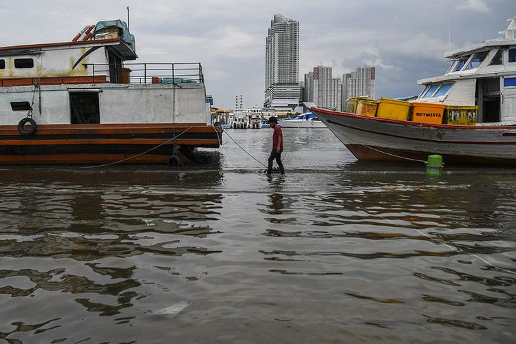 Warga berjalan melintasi banjir rob di Pelabuhan Kali Adem, Muara Angke, Jakarta, Jumat (1/1/2021). Banjir yang terjadi sejak Kamis (31/12/2020) itu dikarenakan pasang surut air laut.