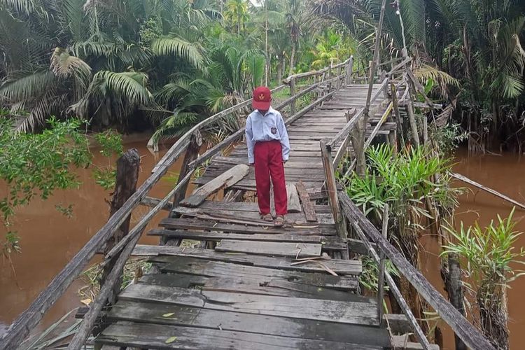 Seorang anak sekolah SD melewati jembatan kayu yang sudah lapuk, di Desa Pulau Kecil, Kecamatan Reteh, Kabupaten Indragiri Hilir, Riau, Senin (18/3/2024).