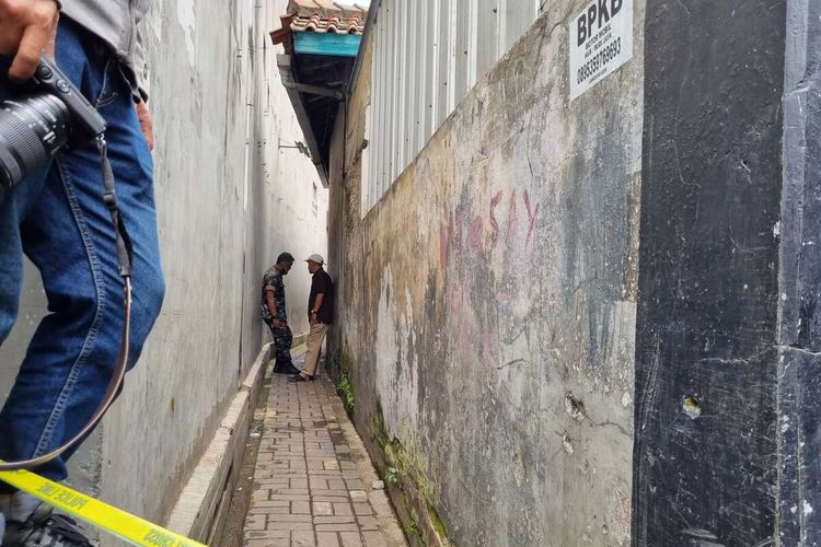 Tampak sebuah gang yang mengarah pada kontrakan temu mayat telah dipasangi garis kuning polisi.