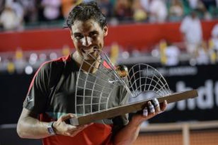 Petenis Spanyol Rafael Nadal menggigit trofi juara setelah mengalahkan Alexandr Dolgopolov dari Ukraine pada final turnamen di Rio de Janeiro, Brasil, Minggu (23/2/2014).