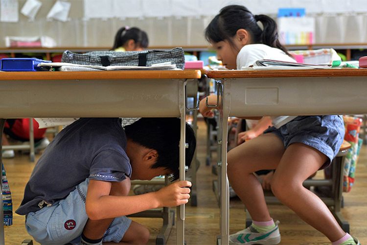 Anak-anak sekolah dasar bersiap untuk berlindung di bawah meja mereka selama latihan gempa di sebuah sekolah di Tokyo pada tanggal 2 September 2013. Latihan anti-bencana nasional diadakan pada tanggal 1 September pada peringatan gempa bumi besar tahun 1923 yang menewaskan lebih dari 140.000 orang di wilayah Tokyo. FOTO AFP / Yoshikazu TSUNO
