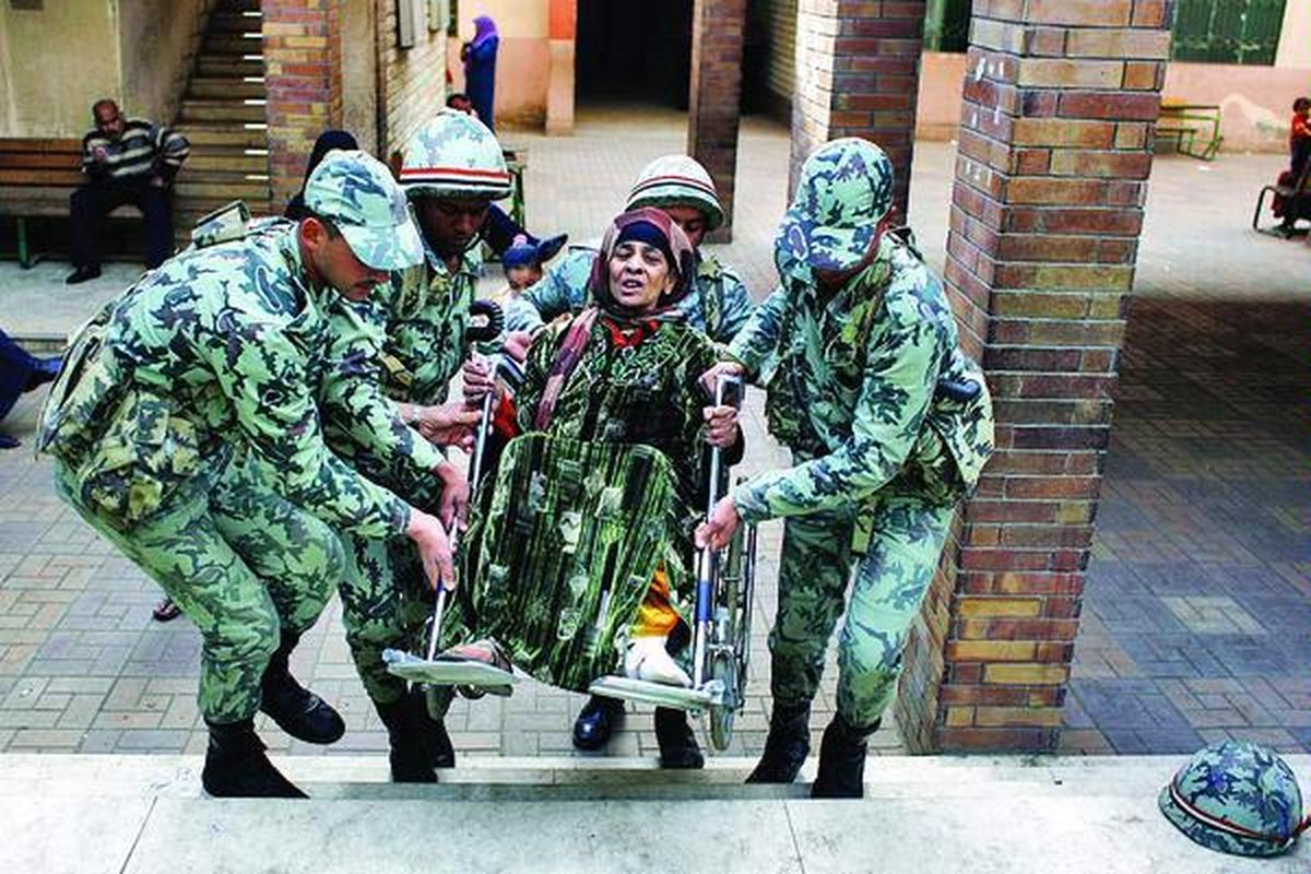 Tentara Mesir menggotong Zeinab al-Shogery (58) di atas kursi rodanya ketika meninggalkan tempat pemungutan suara di Giza, Mesir, Rabu (21/12). Pemungutan suara untuk memilih anggota parlemen Mesir setelah mundurnya Presiden Hosni Mubarak berakhir kemarin, tanpa antrean panjang pemilih di tempat-tempat pemungutan suara.