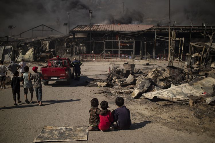 Anak-anak duduk di tanah di kamp yang terbakar di Moria di pulau Lesbos setelah kebakaran besar terjadi, pada 9 September 2020. Ribuan pencari suaka di pulau Lesbos Yunani melarikan diri untuk hidup mereka pada 9 September 2020 sebagai a kebakaran besar melanda kamp Moria, fasilitas migran terbesar dan paling terkenal di negara itu. Lebih dari 12.000 pria, wanita dan anak-anak berlari dengan panik keluar dari kontainer dan tenda dan ke kebun zaitun dan ladang yang bersebelahan saat api menghancurkan sebagian besar kamp yang penuh sesak dan kumuh. Kebakaran dimulai hanya beberapa jam setelah kementerian migrasi mengatakan bahwa 35 orang dinyatakan positif di kamp.