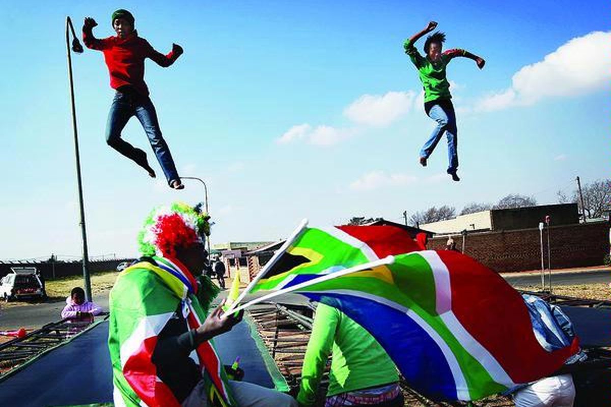 Pedagang pernik-pernik Piala Dunia menjajakan bendera Afrika Selatan di dekat anak-anak yang tengah bermain di atas trampolin di Soweto, Afrika Selatan, Kamis (10/6), 24 jam menjelang dimulainya secara resmi pertandingan sepak bola Piala Dunia 2010.