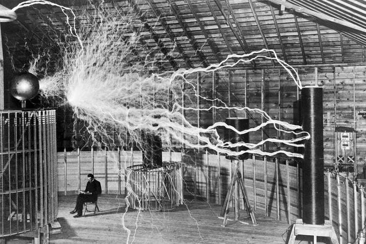 Nikola Tesla duduk saat sedang mengamati temuannya yaitu Tesla coil