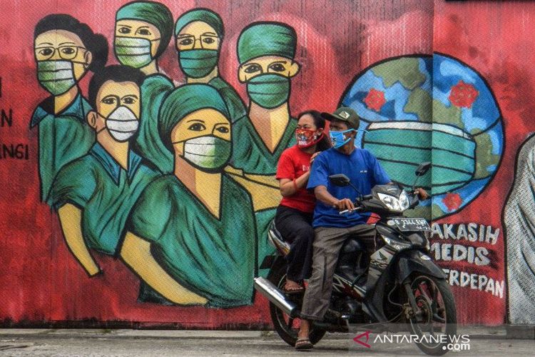 Pengendara motor melintas di depan mural tentang pandemi virus corona atau COVID-19 di Jalan Raya Jakarta-Bogor, Depok, Jawa Barat, Jumar (3/4/2020). Mural tersebut ditujukan sebagai bentuk dukungan kepada tenaga medis yang menjadi garda terdepan dalam menghadapi COVID-19 di Indonesia. 