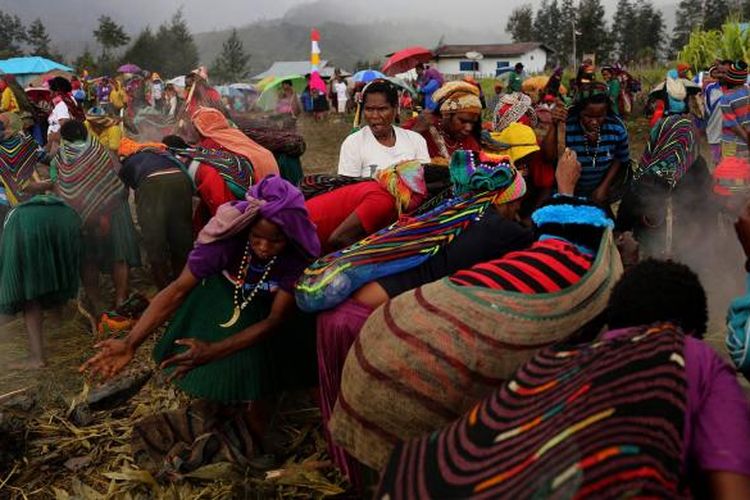 Warga bersama-sama mengangkat batu untuk mengambil makanan yang dimasak dengan bakar batu di Lapangan Trikora, Distrik Ilaga, Kabupaten Puncak, Papua, Kamis (15/9/2016). Tradisi bakar batu merupakan salah satu tradisi terpenting di Papua yang berfungsi sebagai tanda rasa syukur, menyambut tamu, atau acara perdamaian setelah perang antar suku.