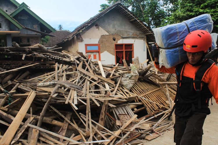 Volunteers pass through the ruins of a house in Malang, East Java that was brought down by a 6.1 Richter scale earthquake in the area on Saturday, (10/4/2021)