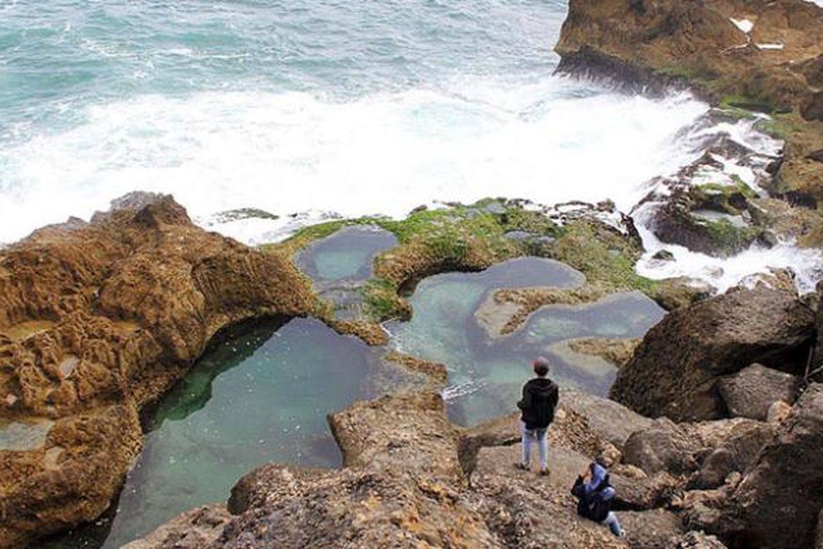 Dua  wisatawan tengah menikmati panorama Pantai Kedung Tumpang di Pucanglaban, Kabupaten Tulungagung, Jawa Timur, Jumat (14/8/2015) sore. Kondisi pantai yang alami, deburan ombak, dan kolam-kolam alami di atas hamparan karang menjadi pesona yang menakjubkan  wisatawan meski infrastruktur masih minim.