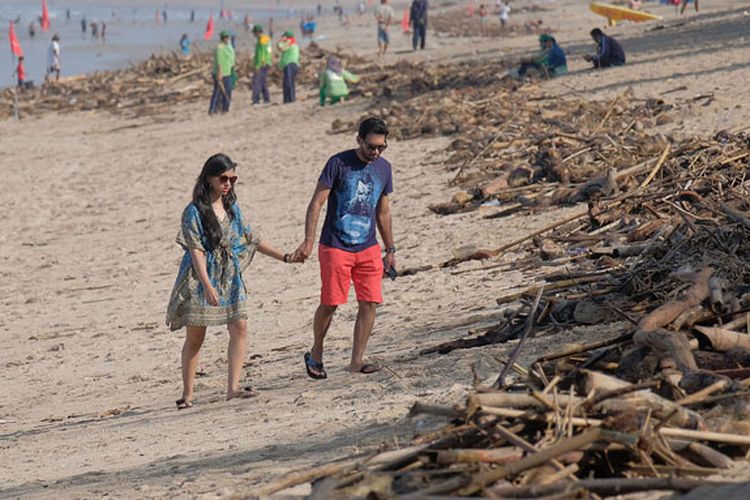 Wisatawan mancanegara melintas di dekat sampah yang terdampar akibat cuaca buruk di Pantai Kuta, Badung, Bali, Senin (11/2/2019). Hujan deras disertai angin kencang yang melanda Bali berdampak pada arus laut yang terus membawa sampah dari daerah lain dan terdampar sejumlah pantai bagian selatan Bali.  