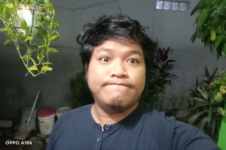 Hasil foto kamera selfie 5 MP (f/2.4) Oppo A16k. Bisa dilihat, detail dan kontur wajah masih bisa terlihat dengan jelas meski foto diambil di kondisi malam hari. Obyek-obyek di sekitar wajah manusia, seperti tanaman dan lain sebagainya, juga masih tampil dengan cukup jelas. 