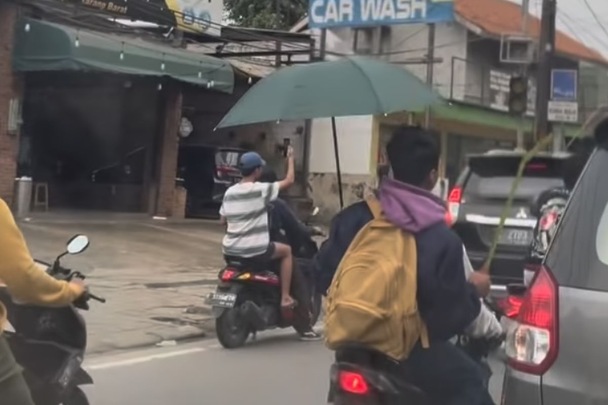 Bidikan layar remaja yang berani tawuran tapi takut hujan melarikan diri ke sela-sela barisan kendaraan menggunakan payung dengan tangan kirinya, sambil menenteng besi panjang di tangan kanannya di Cikarang Barat, Kabupaten Bekasi.