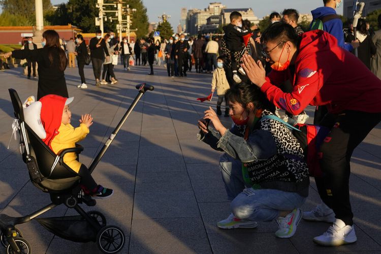 Seorang anak di kereta bayi bereaksi terhadap fotonya yang diambil di dekat Gerbang Tiananmen di Beijing, China, Jumat, 15 Oktober 2021. 