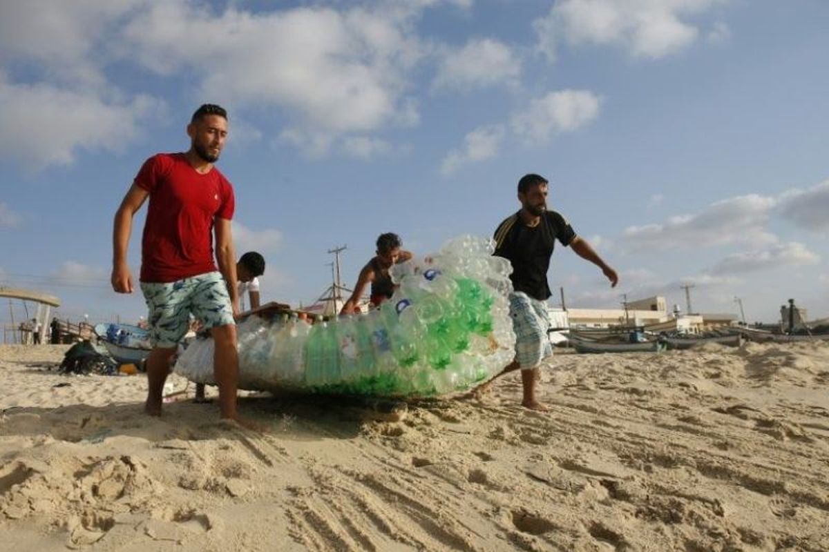 Nelayan Palestina bernama Mouad Abu Zeid (kanan) dan rekan-rekannya membawa perahu yang terbuat dari 700 botol plastik kosong di sebuah pantai di Rafah di Jalur Gaza selatan, Selasa (14/8/2018). (AFP/Said Khatib)