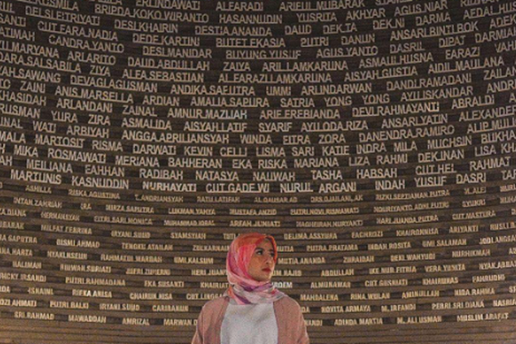 Influencer Karin Novilda atau Awkarin sedang berdiri di depan dinding Sumur Doa yang ada di dalam Museum Tsunami Aceh