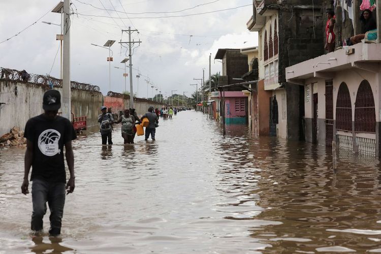 Orang-orang berjalan di jalan yang banjir setelah dua hari hujan lebat yang menyebabkan sungai meluap dan merusak rumah, di Cap-Haitien, Haiti, Selasa (1/2/2022).