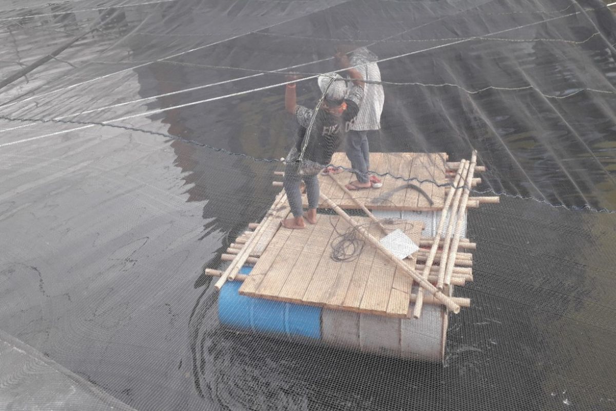 Dua orang pekerja melintas di bawah jaring berwarna hitam yang menutupi Kali Item dekat Wisma Atlet Kemayoran, Kamis (19/7/2018). 