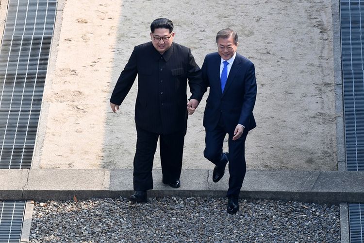 Pemimpin Korea Utara Kim Jong Un (kiri), dan Presiden Korea Selatan Moon Jae In ketika melintasi garis pembatas militer dan kemudian menuju ke Rumah Perdamaian, lokasi Konferensi Tingkat Tinggi (KTT) Antar-Korea di Panmunjom, Jumat (27/4/2018).