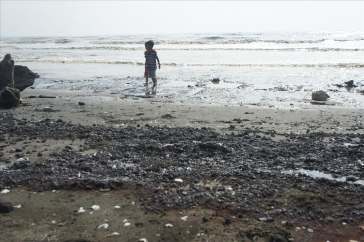 Anak-anak tengah bermain di dekat tumpahan minyak di pantai Desa Cemarajaya, Kecamatan Cibuaya, Kabupaten Karawang, Senin (22/7/2019).

