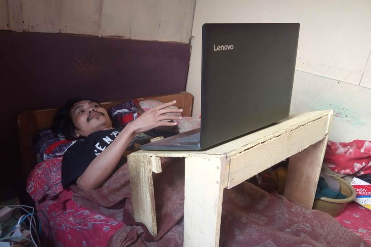 Febri, 17 tahun terbujur kaku di kasur. Untuk mengisi waktu dia bermain laptop.