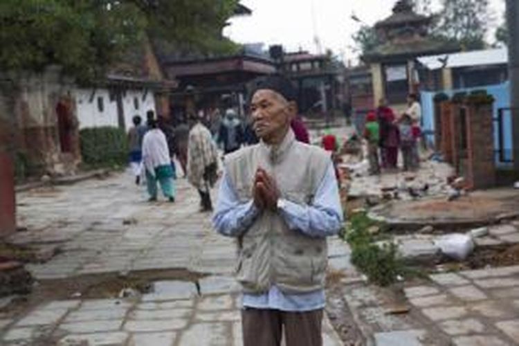 Seorang warga berdoa di antara bangunan yang hancur akibat diguncang gempa bumi di Kathmandu, Nepal, 26 April 2015. Gempa tektonik berkekuatan 7.9 SR mengguncang Nepal pada 25 April, mengakibatkan ribuan orang meninggal.
