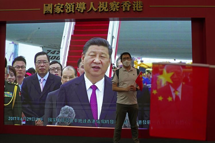 Seorang pengunjung berpose di depan TV yang menunjukkan presiden China Xi Jinping di sebuah pameran untuk menandai peringatan 25 tahun kembalinya bekas jajahan Inggris ke pemerintahan China, di Hong Kong, Jumat, 24 Juni 2022. Pada Selasa (3/1/2023), Pemerintah China mengecam aturan pembatasan Covid-19 baru yang diberlakukan bagi pelancong dari negaranya oleh belasan negara di dunia.