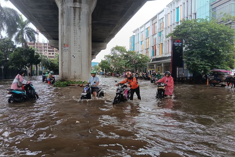 Sejumlah pengendara motor yang terjebak banjir memilih untuk mendorong kendaraan mereka di  Jalan Boulevard Timur, Pegangsaan Dua, Kecamatan Kelapa Gading, Jakarta Utara. Minggu (18/1/2026).