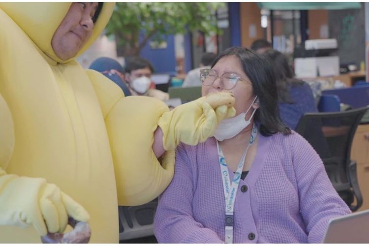 Orang berkostum kuning memaksa karyawan KlikDokter memakan donat. 