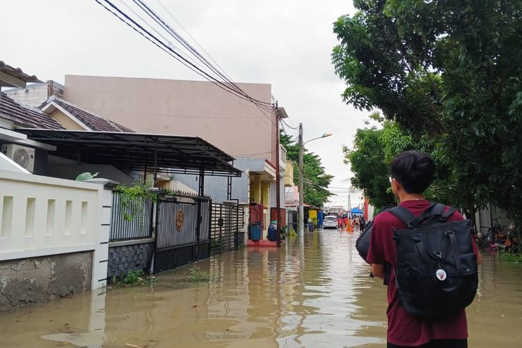 Reporter Kompas.com, Manda Firmansyah, berjalan meninggalkan rumahnya untuk mengungsi akibat banjir di Kelurahan Bahagia, Kecamatan Babelan, Kabupaten Bekasi, Senin (19/1/2026).