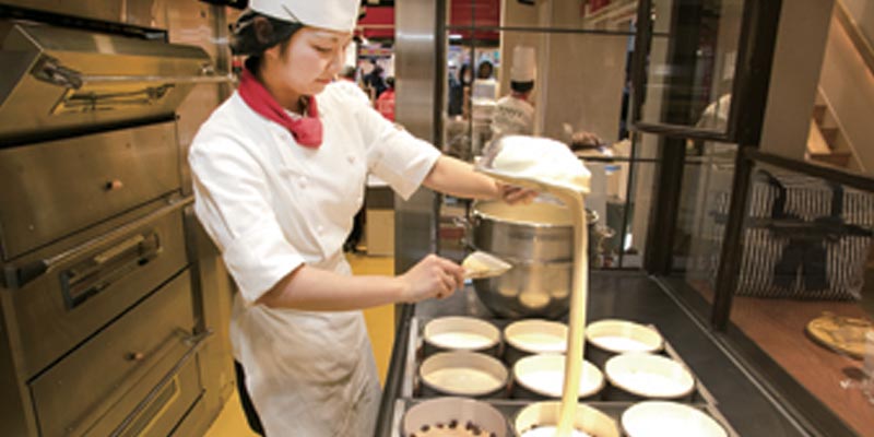 Proses pembuatan cheesecake di Osaka, Jepang. Setelah selesai diaduk, adonan dimasukkan ke dalam masing-masing loyang kertas dari jarak yang cukup tinggi.