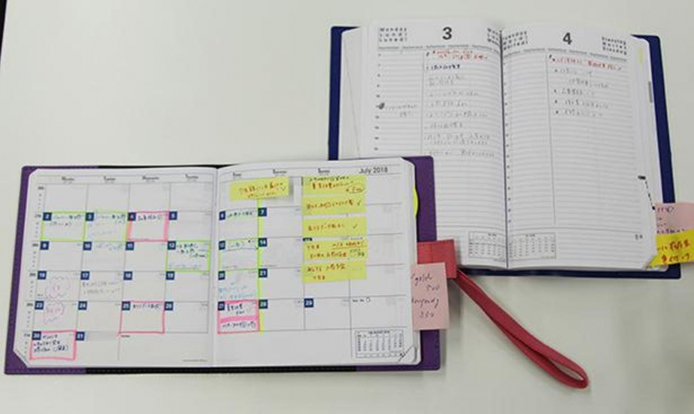Seorang pegawai perempuan penanggung jawab logistik menggunakan dua buku agenda monthly/bulanan dan daily/harian, dan mengisinya jadwal maupun To-Do list.