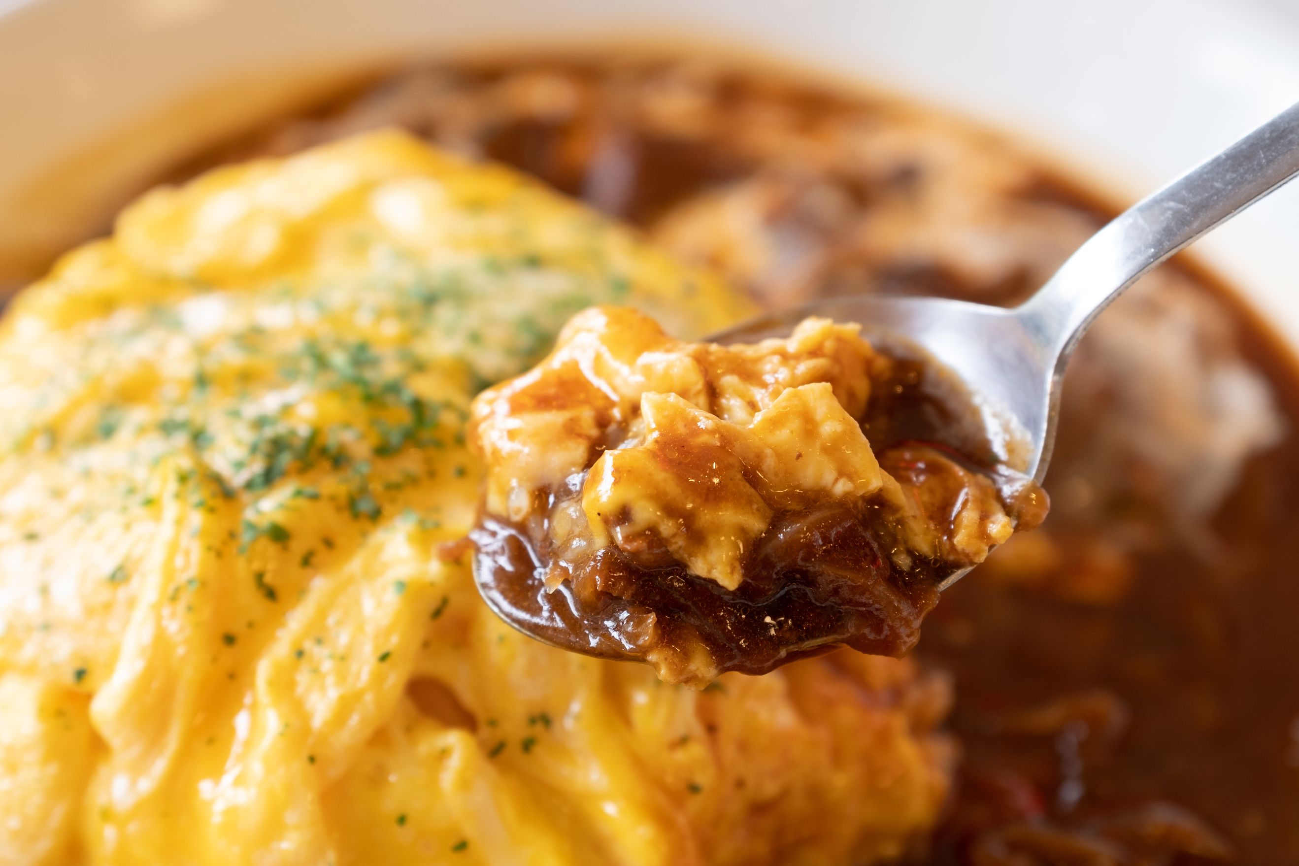 Close up the Spoon with Japanese Omu rice (Omelette or egg) on top with Demi-glace sauce or Curry sauce on white plate over wooden table. Ready to eat