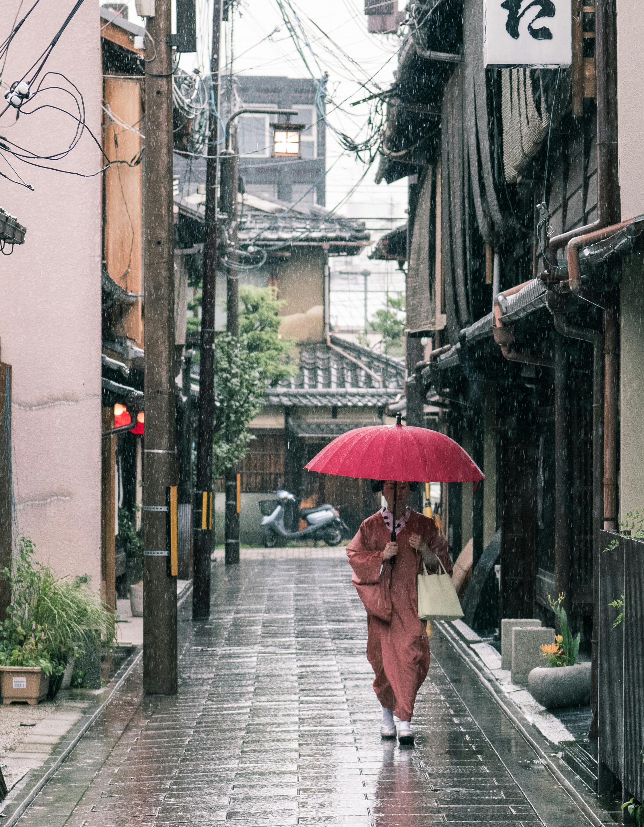 Seorang perempuan yang mengenakan pakaian tradisional Jepang sedang menggunakan payung.