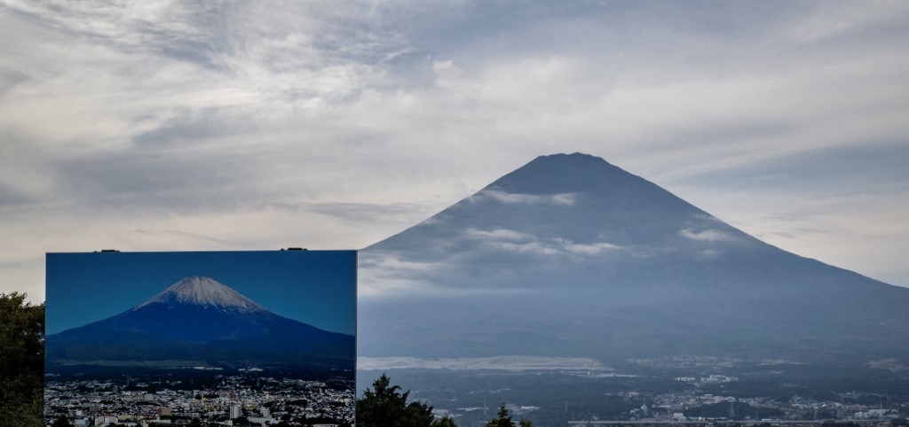 Penampakan puncak Gunung Fuji masih belum bersalju sampai 31 Oktober 2024 yang terilhat dari Gotemba, Prefektur Shizuoka (belakang). Foto bagian depan menunjukkan sebuah tanda bergambar Gunung Fuji dengan puncak bersalju.