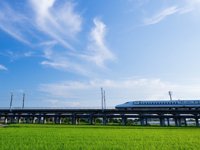 Ilustrasi shinkansen sedang melaju dengan latar belakang langit biru.