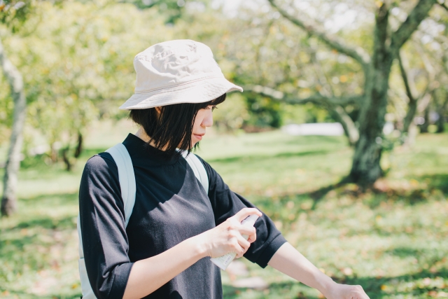 Seorang wanita mengenakan outfit kaos dan topi sedang mengaplikasikan sunscreen.