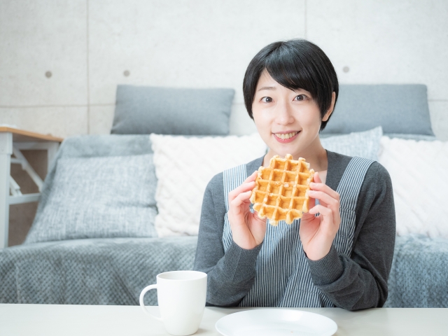 Seorang wanita memakai outfit kaos santai sedang menikmati snack.