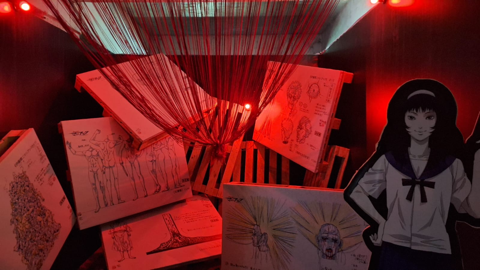 Salah satu bagian pameran di jalur C menampilkan lukisan yang dihiasi benang merah serta standee karakter dari karya Junji Ito, dengan perpaduan tone warna yang kelam dan mencekam, sejalan dengan ciri khas tema horor sang seniman.
