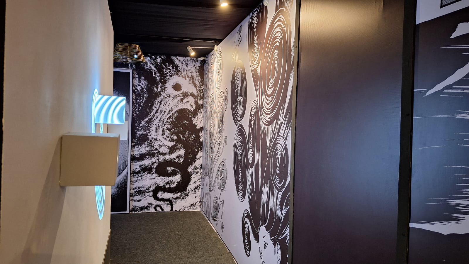 Lorong sempit yang dipenuhi lukisan dengan tone warna gelap dan nuansa horor yang khas dari gaya artistik Junji Ito.