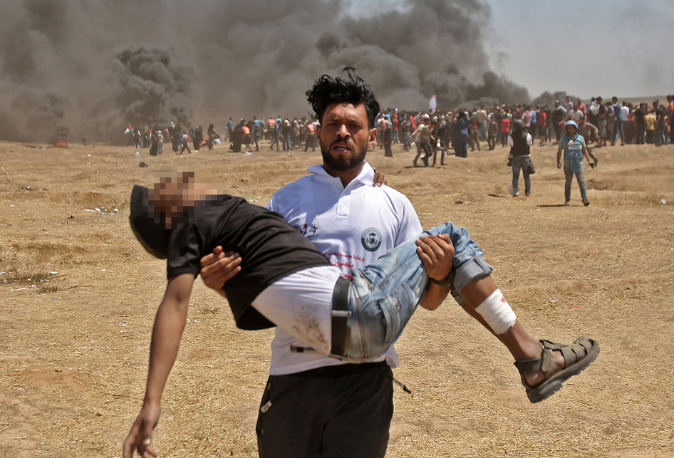 Warga Palestina mengangkat seorang korban saat terjadi bentrokan dengan pasukan Israel di dekat perbatasan antara jalur Gaza dan Israel, di sebelah timur Kota Gaza, Senin (14/5/2018). Otoritas Palestina menyebut pasukan Israel telah menewaskan 55 orang dan melukai 2.700 orang dalam aksi protes dan bentrokan menentang pembukaan Kedutaan Besar Amerika Serikat di Yerusalem.. (AFP PHOTO/MAHMUD HAMS)
