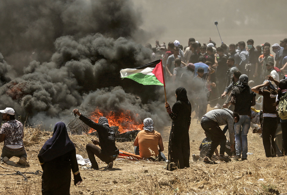Seorang perempuan warga Palestina memegang bendera negaranya saat terjadi bentrokan dengan pasukan Israel di dekat perbatasan antara jalur Gaza dan Israel, di sebelah timur Kota Gaza, Senin (14/5/2018). Otoritas Palestina menyebut pasukan Israel telah menewaskan 55 orang dan melukai 2.700 orang dalam aksi protes dan bentrokan menentang pembukaan Kedutaan Besar Amerika Serikat di Yerusalem.. (AFP PHOTO/MAHMUD HAMS)