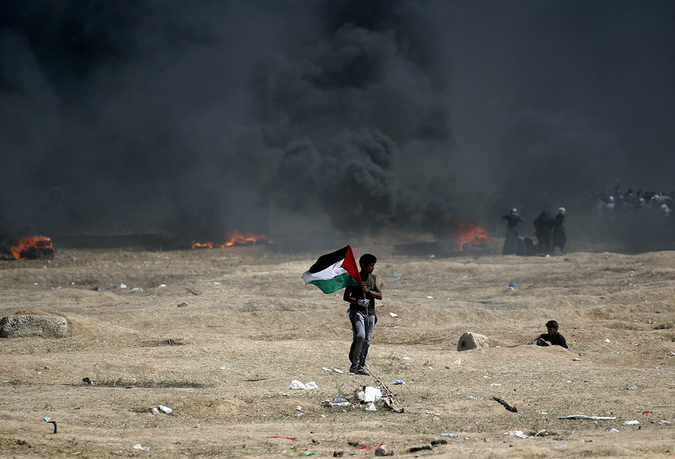Seorang pria warga Palestina memegang bendera negaranya saat terjadi bentrokan dengan pasukan Israel di dekat perbatasan antara jalur Gaza dan Israel, di sebelah timur Kota Gaza, Senin (14/5/2018). Otoritas Palestina menyebut pasukan Israel telah menewaskan 55 orang dan melukai 2.700 orang dalam aksi protes dan bentrokan menentang pembukaan Kedutaan Besar Amerika Serikat di Yerusalem.. (AFP PHOTO/THOMAS COEX)